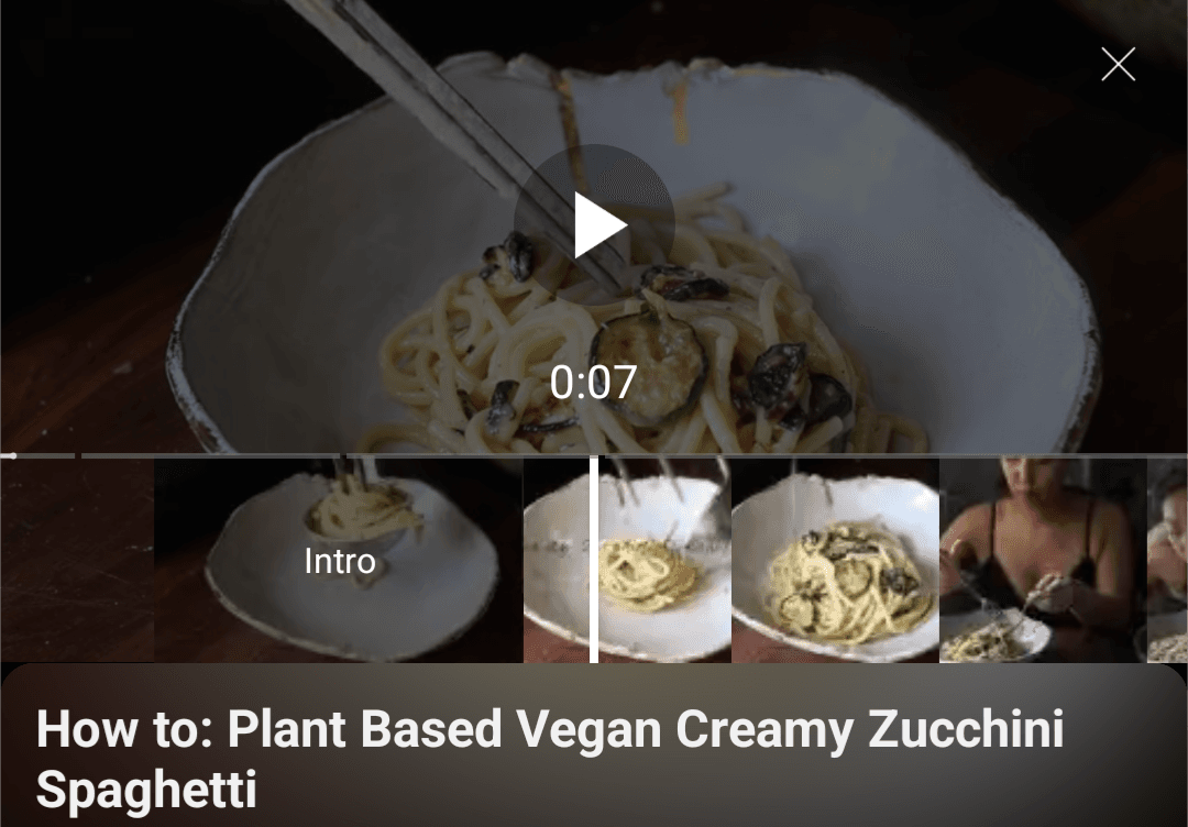 Image represents a video player interface showcasing a recipe.  The top section displays a video preview of creamy zucchini spaghetti in a light-colored bowl, with chopsticks partially visible. A play button is centrally located, and a timer showing '0:07' indicates the video's current position. A small 'x' is in the upper right corner, suggesting a close button. Below the video preview are four smaller thumbnail images, arranged horizontally. The leftmost thumbnail is labeled 'Intro,' depicting a close-up of the spaghetti being served. The next two thumbnails show additional shots of the prepared dish. The final thumbnail on the right shows a person preparing the dish.  At the very bottom, the text 'How to: Plant Based Vegan Creamy Zucchini Spaghetti' describes the video's content. The overall arrangement suggests a social media platform or app displaying a recipe video with preview images and a title.